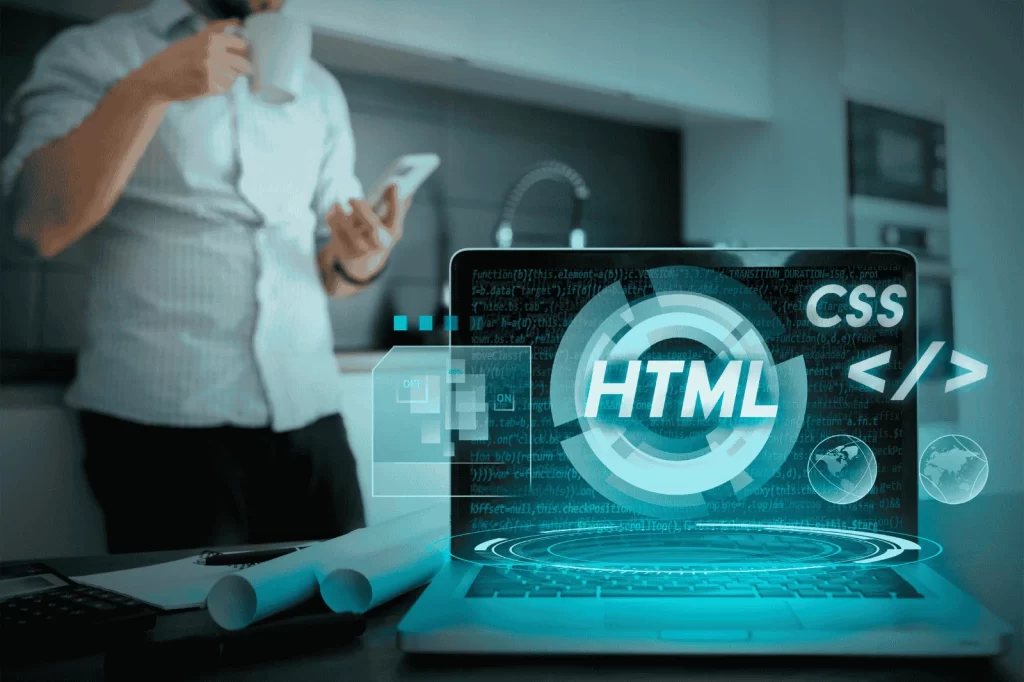 A laptop displaying digital elements related to web development, including "HTML" and "CSS" symbols, with a person in the background holding a phone and a coffee cup.